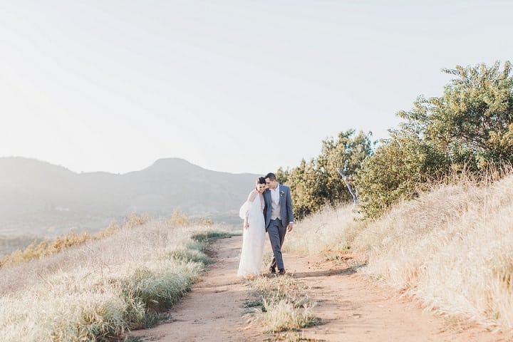 Newlyweds walking through a sunlit hillside landscape